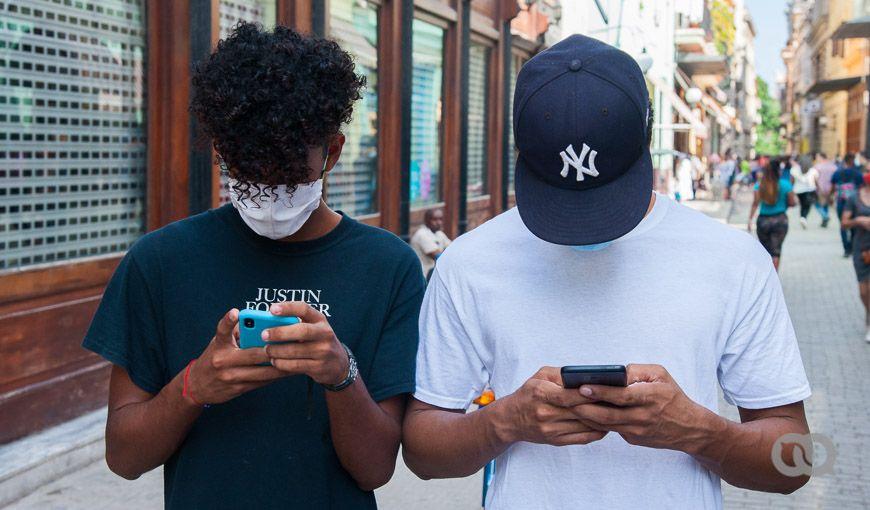 Conexión a Internet en La Habana, dos muchachos mirando sus celulares en la calle, gorra de los yankees. Foto: Verdecia.
