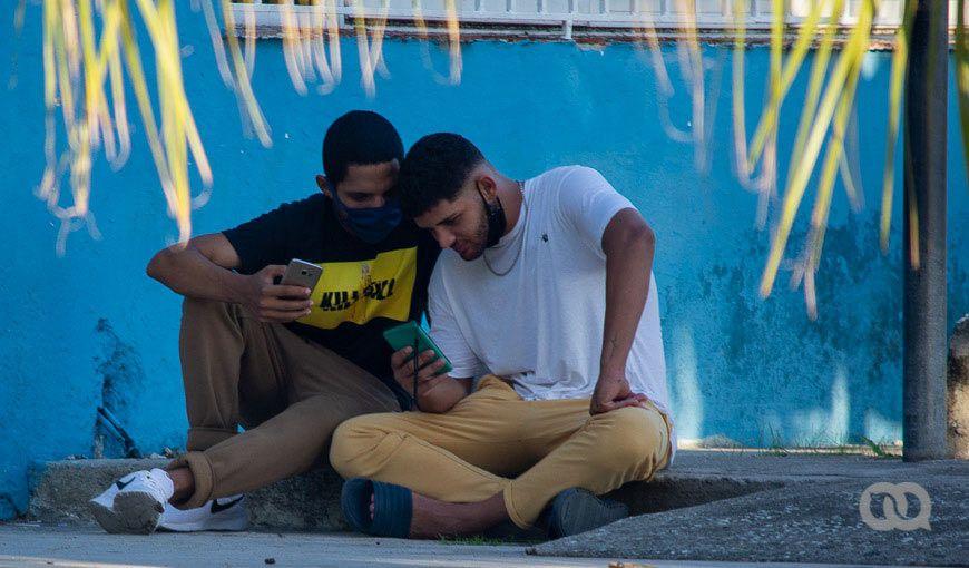 jóvenes cubanos miran celular y debaten sobre criptomonedas y criptoactivos