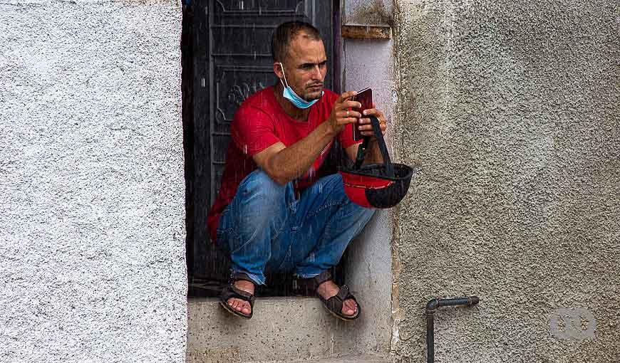 Hombre sostiene su celular en la puerta de la una casa mientras llueve, Cuba.